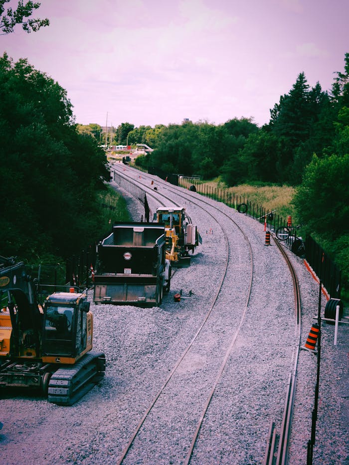 gallery-04 Construction vehicles and railway tracks in a forest setting, showcasing infrastructure development.