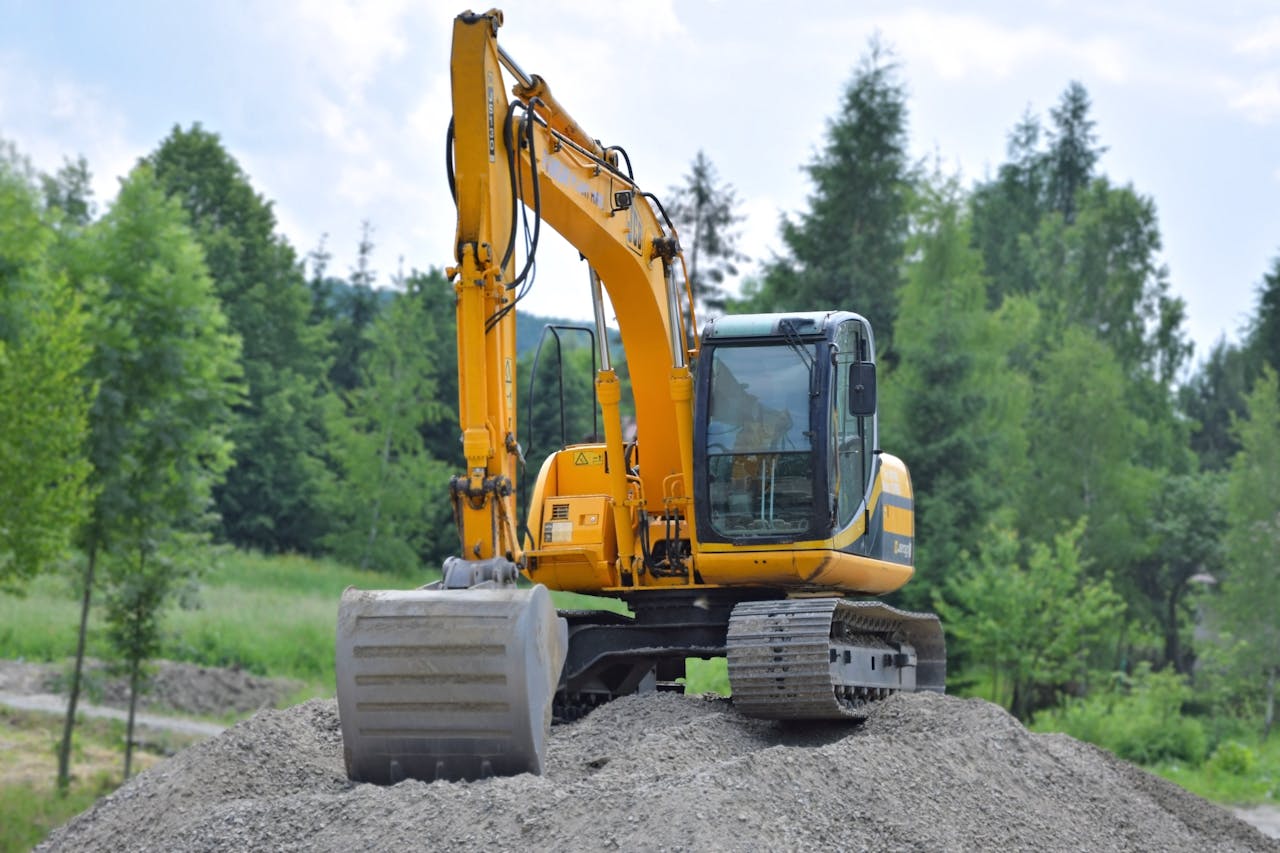 cta-02 A yellow excavator on a pile of gravel in a lush, green forest setting in Poland.